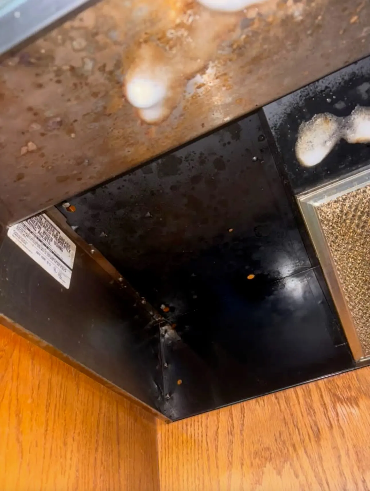 Before: underside of a range hood coated in brown grease, with cleaner foam