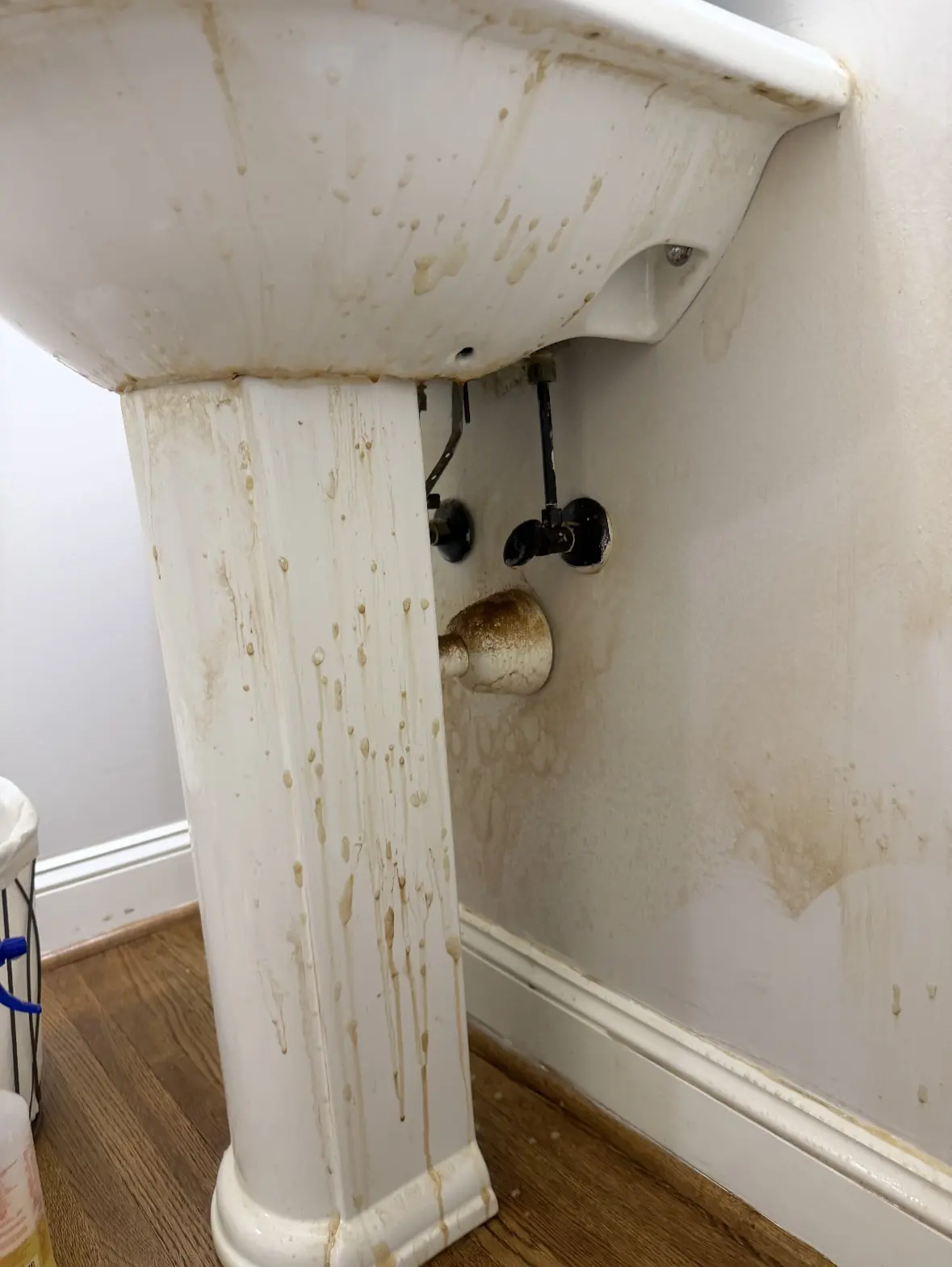 Before: pedestal sink, pipes and wall covered in brown splatter stains
